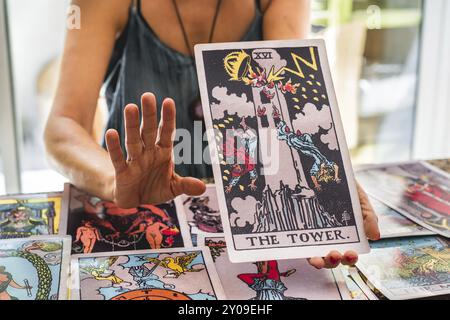 Tarot-Leser zeigt die riesige Tarot-Karte The Tower, während sie ihre Hand hebt, als wolle sie Warten sagen Stockfoto