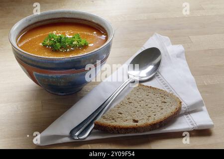 Gemüsesuppe, Tomaten, Karotten oder Kürbis, in einer Töpferschüssel mit Brot und Löffel Stockfoto