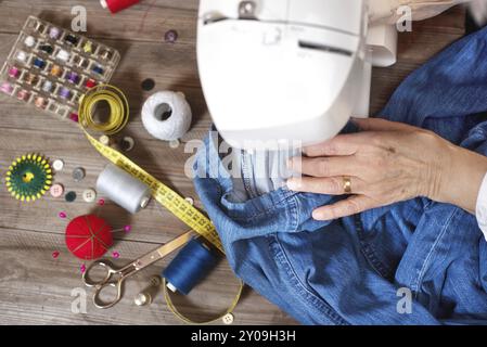 Nahaufnahme von oben, von der Schneiderin der Seniorenhand, die Jeans auf einer elektrischen Nähmaschine Nähte Stockfoto