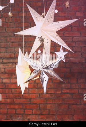 Weiße dekorative Weihnachtssterne in verschiedenen Größen und Formen, die vor rotem Backstein-Hintergrund hängen Stockfoto