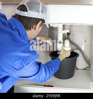 Klempner in Arbeitskleidung, der einen Abfluss repariert Stockfoto