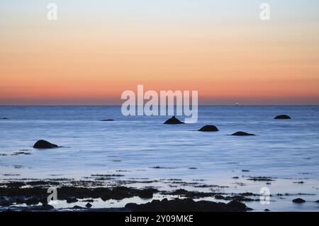 Sonnenuntergang, Steinstrand mit kleinen und großen Felsen vor dem beleuchteten Meer. Lichtwellen. Poelinsel an der Ostsee. Naturfoto von den coas Stockfoto