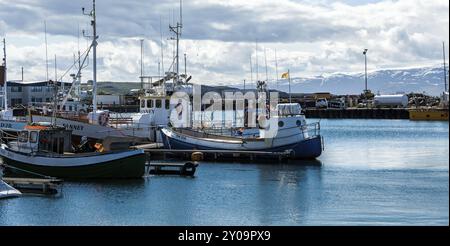 HUSAVIK, ISLAND, 29. JUNI: Ruhiger Hafen mit verankertem Fischerboot und Bergen im Hintergrund am 29. Juni 2013 in Husavik, Island, Europa Stockfoto