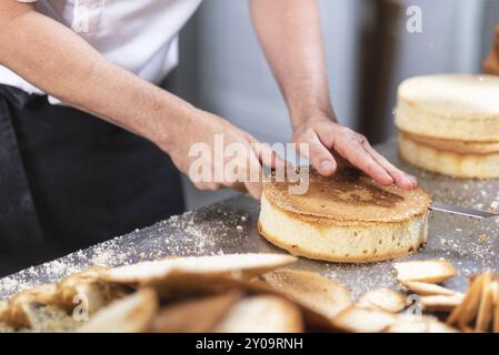 Der Konditor schneidet den Biskuitkuchen in Schichten. Kuchenherstellungsprozess Stockfoto