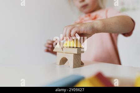 Kleines Mädchen, das zu Hause oder im Kindergarten Holzbausteine spielt. Entwicklungs- und Baukonzept. Mehrfarbige Lernsteine für e Stockfoto