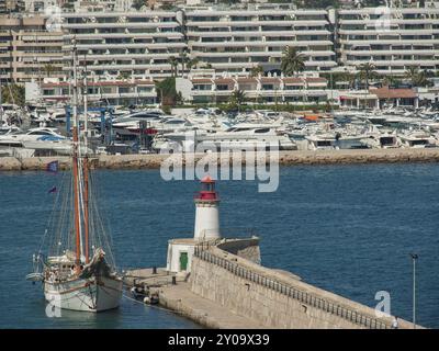 Segelboot und Leuchtturm im Hafen mit zahlreichen Yachten und Küstengebäuden im Hintergrund, ibiza, mittelmeer, spanien Stockfoto