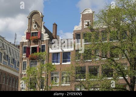 Historische Gebäude mit roten Fensterläden und Blumendekorationen unter blauem Himmel, Amsterdam, Niederlande Stockfoto