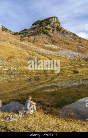 Der Augstsee und der Atterkogel auf dem Verlierer. Ein Wanderer sitzt auf einem Felsen. Herbst, gutes Wetter, blauer Himmel. Reflexion. Altaussee, Bad Aussee, Aus Stockfoto