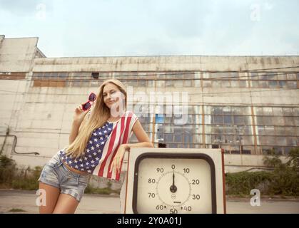 Blondes Mädchen hält die Hand auf ihre Brille auf beschädigte Tankstelle stehend Stockfoto