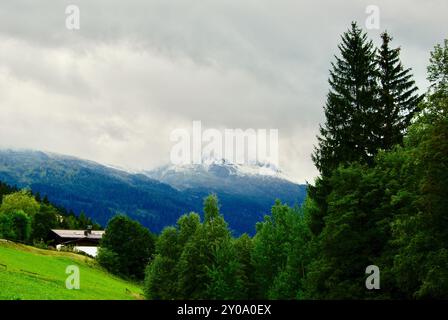 Blick auf eine Berglandschaft mit einem Gebäude am Hang an einem regnerischen Tag mit grauen Wolken und Nebel über den Gipfeln im Herbst in Österreich. Stockfoto