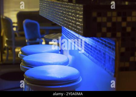 Leere Barhocker an der Bar, blau-lila beleuchtet Stockfoto