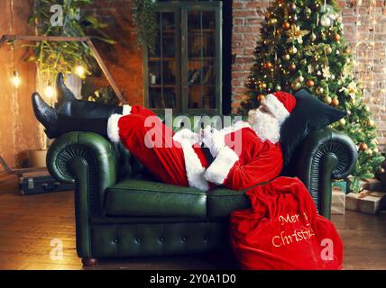 Santa Claus schlafen zu Hause in der Nähe von Weihnachtsbaum auf dem grünen Sofa Stockfoto