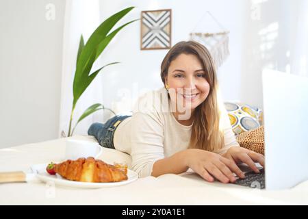 Lächelnd weibliche Freiberufler arbeiten am Laptop und Frühstück im Bett zu Hause. Stockfoto