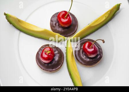 Drei Kirschen auf drei Schokoladenkeksen mit Avocadoscheiben Stockfoto