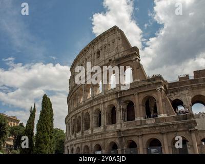 Seitenansicht des imposanten Kolosseums mit hohen Arkaden und Bäumen unter bewölktem Himmel, Rom, Italien, Europa Stockfoto