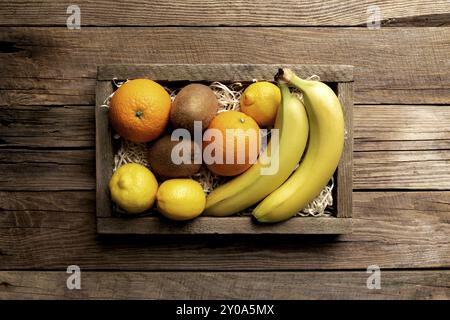 Frische tropische Früchte in einem Holzlieferkarton auf einem Holzhintergrund. Orange, Banane, Kiwi und Zitrone, flach, mit Platz für einige Adver Stockfoto