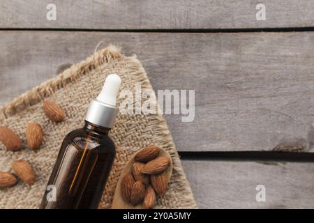 Ätherisches Mandelöl in Glasflasche mit Löffel. Kosmetisches Konzept auf hölzernem Hintergrund mit Sacktuch, isolierte Flachlage. Stockfoto