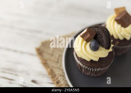 Leckere bunte Muffins und Cupcakes auf einem Tablett, Holzhintergrund. Dekoriert mit verschiedenen Bonbons, Plätzchen, Blaubeeren und farbigen Süßcreme-Cche Stockfoto