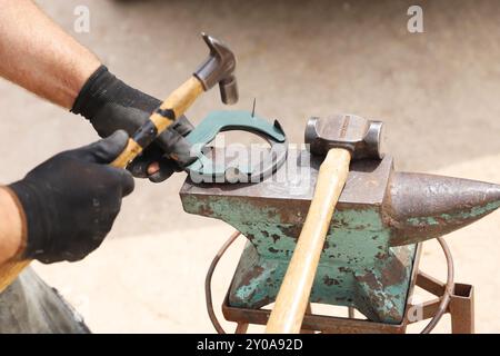 Farrier-Werkzeuge aus nächster Nähe auf der ländlichen Pferdefarm. Hintergrund des Reitsports. Ausrüstung und Hammer ruhen auf dem alten Amboss. Stockfoto