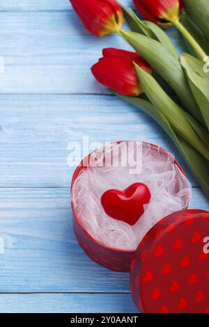 Rotes Herz in einer Box und Tulpen auf blauem Hintergrund aus Holz. Valentinstag Stockfoto