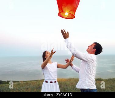 Junges Paar starten eine rote chinesische Himmelslaterne in der Abenddämmerung am Meer Stockfoto
