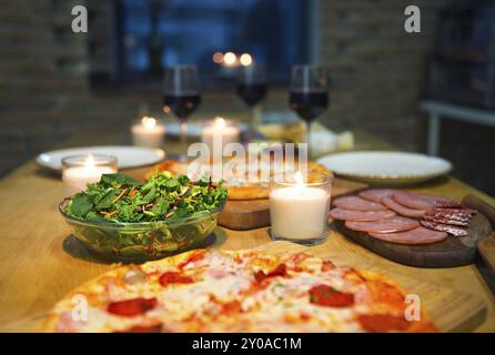 Tabelle mit verschiedenen Lebensmitteln mit Rotwein und Kerzen serviert. Stockfoto