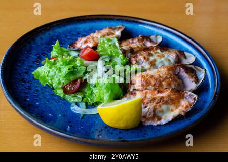 Fisch Und Meeresfrüchte. Muschelmuscheln. Gebackene Muscheln mit Käse, Koriander und Zitrone in Schalen auf gusseiserner schwarzer Platte. Teller mit Muscheln, kaltem Weißwein, Zitrone Stockfoto