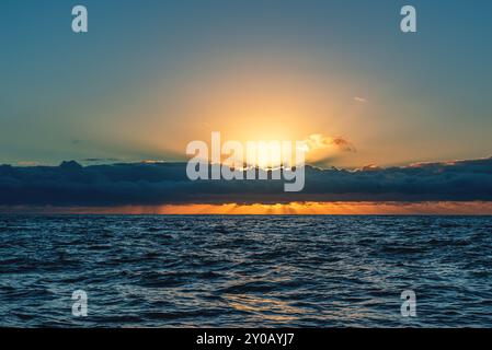 Sonnenaufgang über den wunderschönen hawaiianischen Gewässern während eines wunderschönen, ruhigen morgens, während Wolken helfen, Charakter zu schaffen und wenn die Sonne hinter ihnen aufgeht. Stockfoto