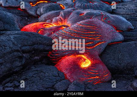 Bei einer Wanderung in die kargen Lavafelder in Hawaii bei Nacht wird eine aktive Eruption beobachtet, bei der Lava durch vorhandene getrocknete Lava strömt und durch die fließt Stockfoto