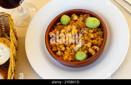 Migas pastoriles aus gebratenem zerbröseltem Brot mit Speck und Chorizo serviert mit Trauben Stockfoto