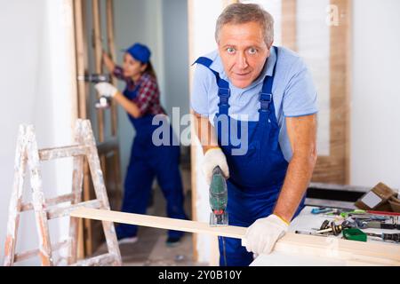 Fokussierter Mann mittleren Alters in einer Blauuniform mit einer Stichsäge auf Holzplanke zu Hause Stockfoto