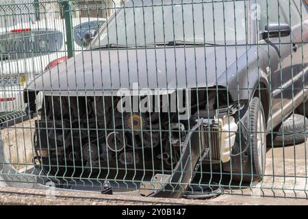 Ein beschädigtes Fahrzeug ohne vorderen Stoßfänger und Motorhaube ist hinter einem Kettenzaun geparkt Stockfoto