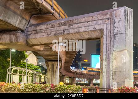 Nachts nähert sich ein obenliegender Personenzug, der über riesige Betonsäulen fährt und die massiven gekrümmten Eisenbahnen unterstützt, die ein geschäftiges stadtzentrum umgeben Stockfoto