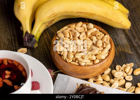 Erdnüsse aus der Schale in einer Holzschale, ein Tisch mit Erdnüssen, Bananen und rotem Tee mit Himbeeren Stockfoto