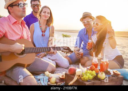 Freunde auf dem Sand am Strand im Kreis sitzen. Ein Mann spielt Gitarre Stockfoto