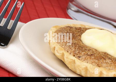 Nahaufnahme einer Mini-Walnuss-Torte mit Mascarpone, ein Dessertgabel und ein Glas Milch auf einem roten Hintergrund Stockfoto