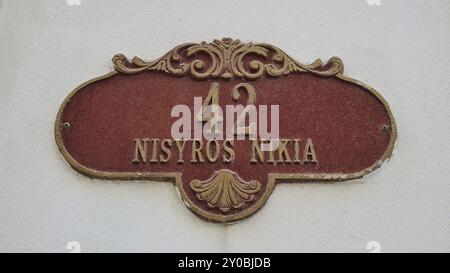 Rot-goldenes Hausnummernschild mit der Aufschrift „42 Nisyros Nikia“ an einer weißen Wand, Platia, Nikia, Nisyros, Dodekanese, Griechische Inseln, Griechenland, Eu Stockfoto