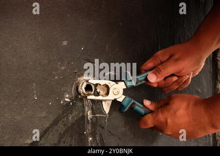 Hand eines asiatischen Klempners, der den Wasserhahn mit einer Zange an der Wand befestigt Stockfoto