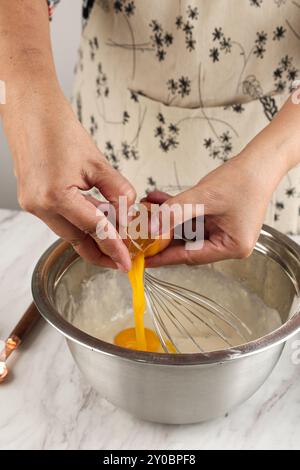 Frauenhände brechen Eier in Staonless Bowl zum Backen auf dem Tisch Stockfoto