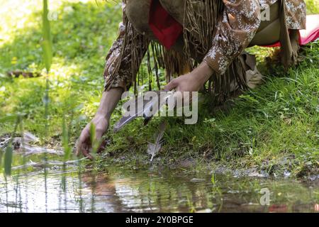 Ein Mann in indischer Kleidung nimmt eine Vogelfeder auf einer Wiese am Ufer eines Baches auf Stockfoto