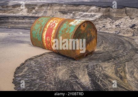 Rostiges Fassöl an einem teilweise schwarzen Strand veranschaulicht die Umweltbelastung durch Ölleckagen Stockfoto