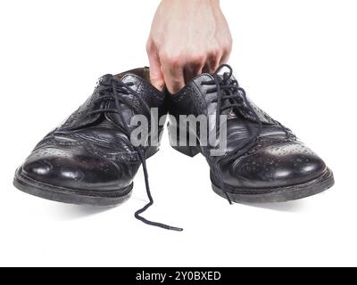 Männliche Hand hält ein Paar abgetragene schwarze Lederschuhe in Richtung weiß Stockfoto