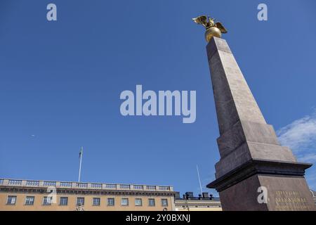 Steinobelisk mit goldener Adlerstatue vor einem Gebäude unter einem hellblauen Himmel, Helsinki, Finnland, Europa Stockfoto