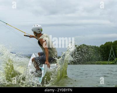 Junger Mann, der mit einem Wakeboard in den See springt, Wassersport, Wasserski im Wakpark Stockfoto