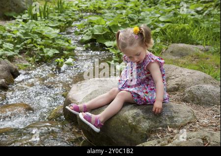 Kleines Mädchen im Sommerkleid, das auf einem Bach sitzt Stockfoto