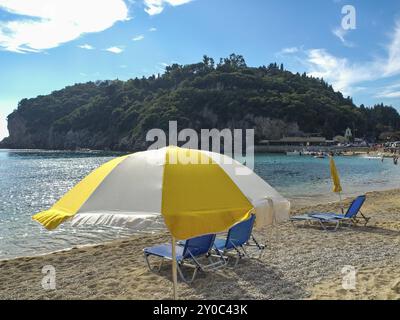 Strand mit gelbem Sonnenschirm und Liegestühlen an einem sonnigen Tag, ruhiges Meer im Hintergrund, korfu, mittelmeer, griechenland Stockfoto