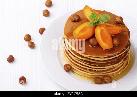 Stapel hausgemachter amerikanischer Pfannkuchen, serviert mit Honig, Haselnüssen und Aprikosen auf weißem Teller Stockfoto