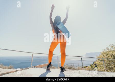 Frau in Orange hebt ihre Arme mit einer Yoga-Matte Stockfoto