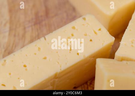 Hartkäse mit Löchern, die auf einem Schneidebrett in dicke Stücke geschnitten werden, große Käsestücke für Pizza und Snacks Stockfoto