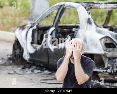 Weinender, verärgerter kaukasier bei einem Verkehrsunfall oder Brandstiftung Feuer verbrannten Rad Auto Auto-Trödel Stockfoto